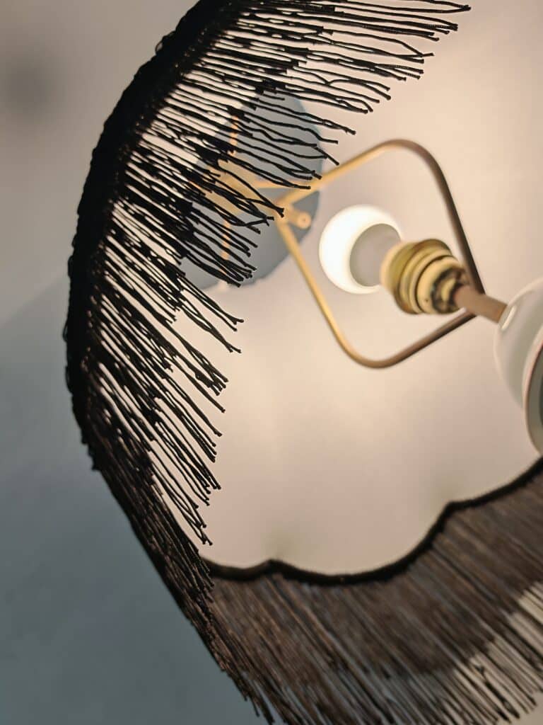 Ambiance Chaleureuse: Lampe Design Abat-jour à Franges Noires Lampe de plafond avec abat-jour à franges noires, révélant une ampoule allumée. Lumière chaude, design intérieur rétro-chic.