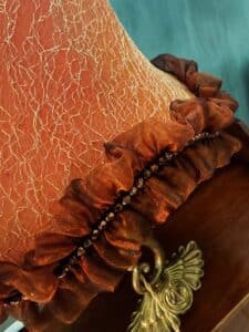 Abat-jour orange au motif doré craquelé, agrémenté d'une bordure en froufrous marron avec perles facettées et un ornement en laiton ailé.