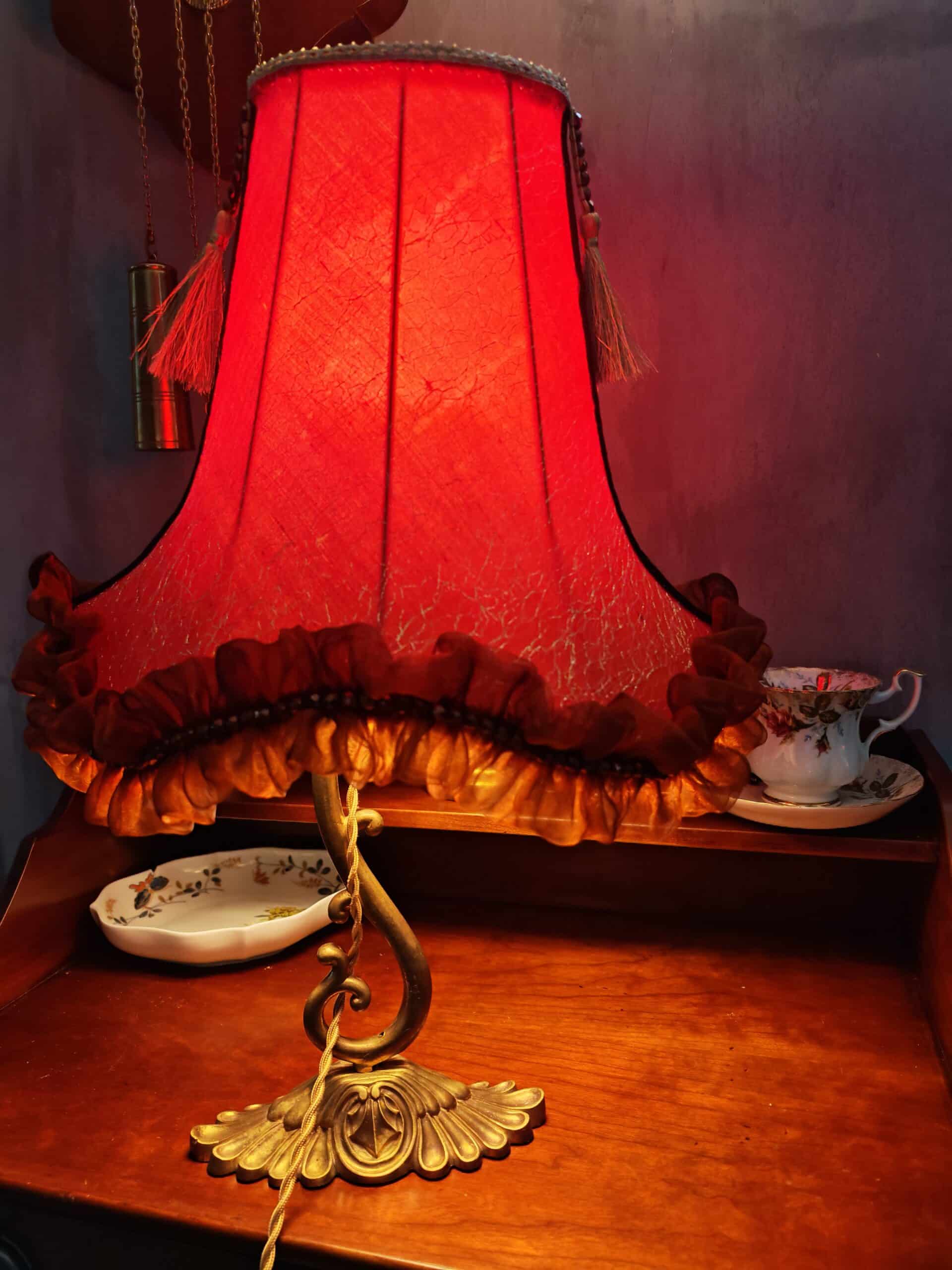 Lampe de table vintage à abat-jour rouge plissé et texturé, base en laiton ornée, sur un meuble en bois foncé avec tasse à thé délicate.