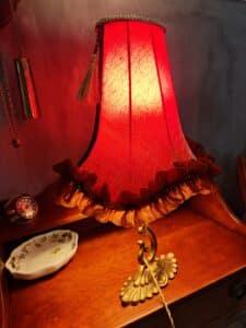 Lampe de table vintage rouge à abat-jour texturé et froncé, base dorée, sur un meuble en bois, près d'une montre gousset et coupelle. Lumière chaude.
