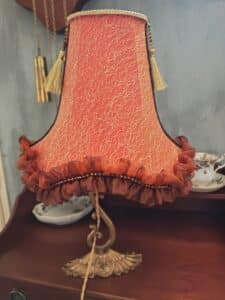 Élégante lampe de table vintage à abat-jour corail texturé doré, ornements perlés et pampilles. Base en laiton sur commode bois.